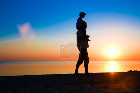 Foto de Padres felices con el niño junto al mar jugar en la silueta de la naturaleza de viaje - Imagen libre de derechos
