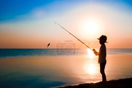Téléchargez les photos : Happy enfant pêcheur pêche par la mer sur la silhouette de la nature Voyage - en image libre de droit