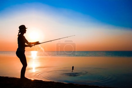 Téléchargez les photos : Happy girl pêcheur attrape des poissons par la mer sur la nature silhouette Voyage - en image libre de droit