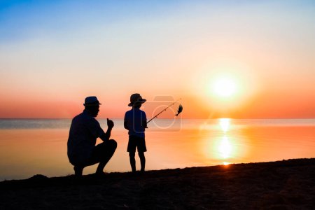 Téléchargez les photos : Père heureux et les enfants pêcheurs pêchent des poissons par la mer sur la silhouette de la nature Voyage - en image libre de droit