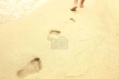 Foto de Viaje a la playa - mujer relajante caminando en una playa de arena dejando huellas en el detalle de arena de los pies femeninos en la playa de arena dorada en Grecia - Imagen libre de derechos