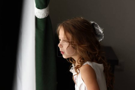 Téléchargez les photos : Petite fille heureuse regarder par la fenêtre - en image libre de droit