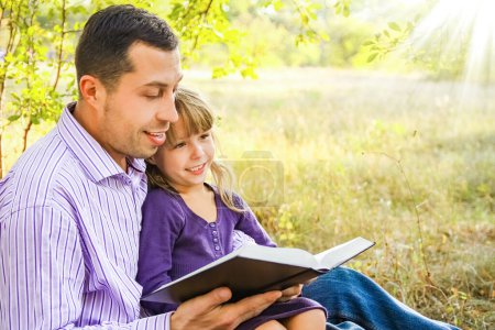 Téléchargez les photos : Jeune père avec une petite fille lisant la Bible - en image libre de droit
