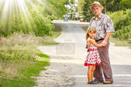 Foto de Feliz abuelo con su nieta en la naturaleza en el parque ir a lo largo del camino de viaje - Imagen libre de derechos