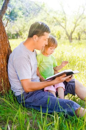 Photo for Happy father with a child reading a book on the nature of the Bible - Royalty Free Image