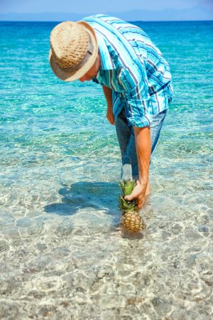 Foto de Hombre feliz con una piña en sus manos cerca del mar en la naturaleza viaje de fin de semana - Imagen libre de derechos