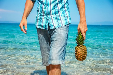 Téléchargez les photos : Homme heureux avec un ananas dans ses mains près de la mer dans la nature week-end Voyage - en image libre de droit