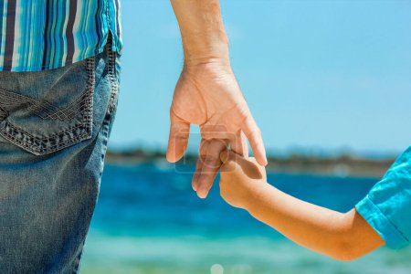 Téléchargez les photos : Heureux papa tient la main d'un enfant par la mer grecque dans la nature - en image libre de droit
