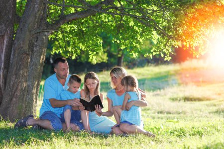 Foto de Feliz familia leyendo la biblia en la naturaleza - Imagen libre de derechos