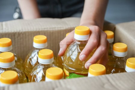 Téléchargez les photos : De nombreuses bouteilles d'huile de tournesol en boîte avec fond de main des gens - en image libre de droit