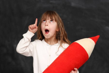 Photo for Little girl student emotions  with a big pencil on black background - Royalty Free Image