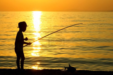 Foto de Feliz niño pescando por la silueta del mar - Imagen libre de derechos