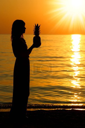 Téléchargez les photos : Heureux fille homme et ananas dans les mains silhouette par la mer Voyage - en image libre de droit