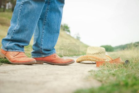 Téléchargez les photos : Jambes de cow-boy dans des chaussures dans le parc sur fond de nature. L'homme du ranch. - en image libre de droit
