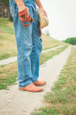 Téléchargez les photos : Jambes de cow-boy dans des chaussures dans le parc sur fond de nature. L'homme du ranch. - en image libre de droit
