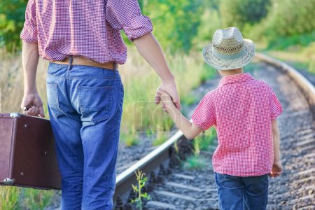 Téléchargez les photos : Mains de parent et fils en chapeau de cow-boy près de la voie ferrée avec valise - en image libre de droit