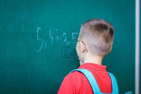 Foto de Niño feliz de pie en la pizarra con una mochila escolar con gafas - Imagen libre de derechos