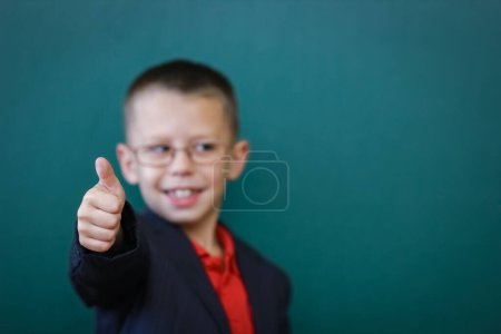 Téléchargez les photos : Enfant heureux debout au tableau noir avec un sac à dos d'école portant des lunettes - en image libre de droit