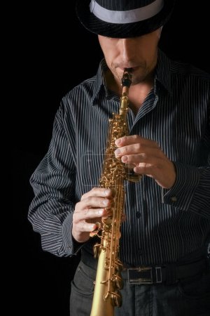 Téléchargez les photos : Saxophone soprano dans les mains d'un mec sur fond noir - en image libre de droit