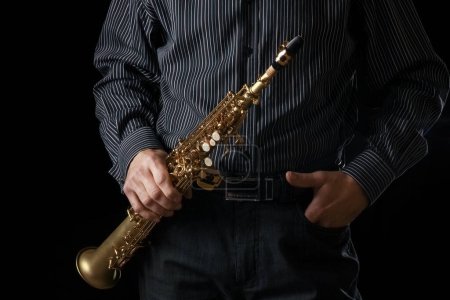 Téléchargez les photos : Saxophone soprano dans les mains d'un mec sur fond noir - en image libre de droit