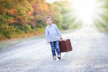 Téléchargez les photos : Enfant heureux avec une valise sur la route dans le parc Voyage - en image libre de droit
