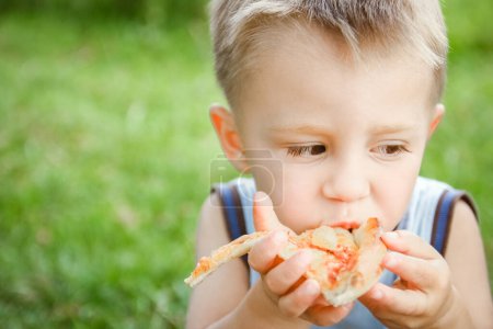 Photo for Child eating a tasty pizza on the nature of the grass in the park - Royalty Free Image