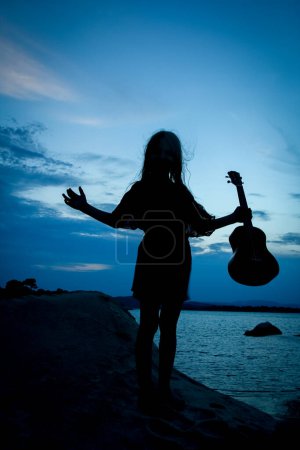 fille heureuse avec ukulele par la mer sur fond de silhouette nature
