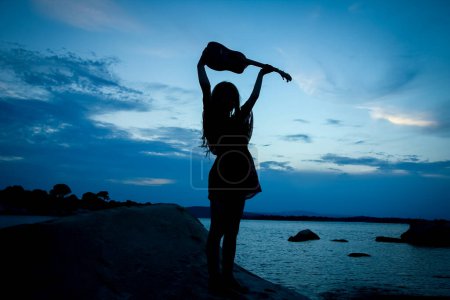 Téléchargez les photos : Fille heureuse avec ukulele par la mer sur fond de silhouette nature - en image libre de droit