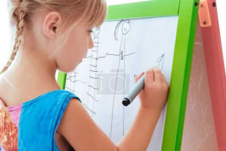 Téléchargez les photos : Heureux enfant dessine sur chevalet sur un fond blanc - en image libre de droit