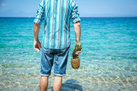 Foto de Hombre feliz con una piña en sus manos cerca del mar en la naturaleza viaje de fin de semana - Imagen libre de derechos