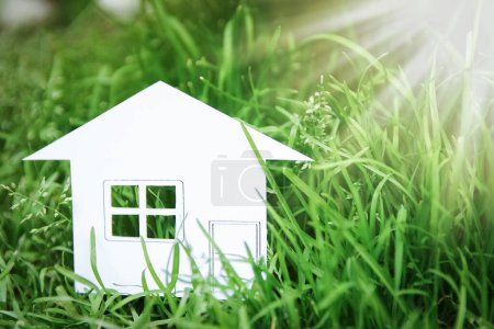 Téléchargez les photos : Le concept ou le livre blanc conceptuel de maison dans sa main dans une herbe verte d'été sur un fond, un symbole pour la construction, l'environnement, le crédit, la propriété ou la maison - en image libre de droit