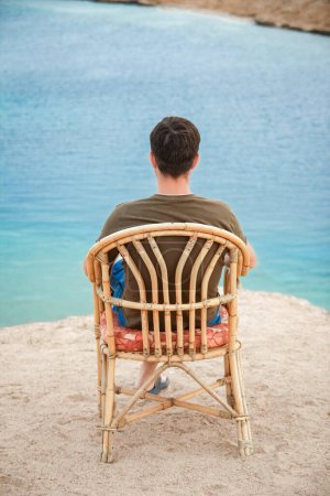 Foto de Chico feliz sentado en un taburete junto al fondo del mar en la naturaleza - Imagen libre de derechos