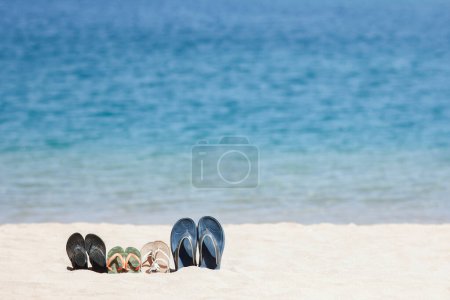 Téléchargez les photos : Pantoufles de toute la famille dans le sable par la mer sur la nature tout en voyageant. Repos au bord de l'eau en vacances avec des chaussures
. - en image libre de droit