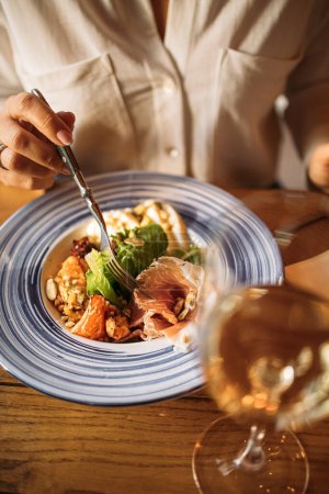 Téléchargez les photos : Une personne mange une salade avec un verre de vin blanc à la table du restaurant - en image libre de droit