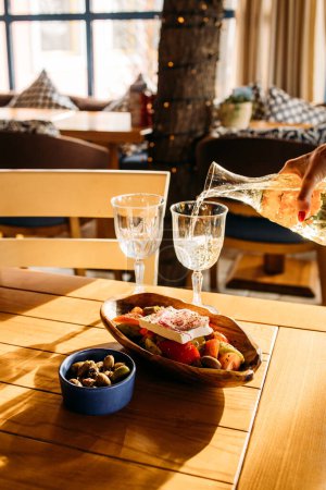 Foto de Ensalada griega servida con aceitunas y dos copas de vino blanco en la taberna - Imagen libre de derechos