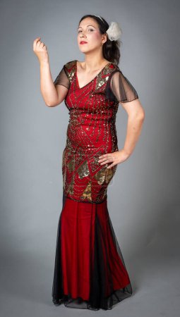 Foto de Mujer en vestido de aleta de lentejuelas rojas posa elegantemente con una mano levantada y la otra en su cadera mirando a la cámara - Imagen libre de derechos