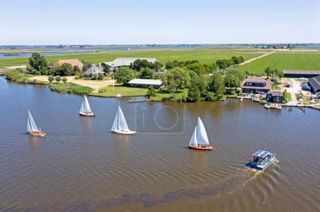 Téléchargez les photos : Aérien de sports nautiques et un ferry à vélo dans la campagne de Frise aux Pays-Bas - en image libre de droit