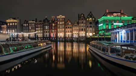 Téléchargez les photos : Maisons médiévales et bateaux de croisière au Damrak à Amsterdam les Pays-Bas la nuit - en image libre de droit