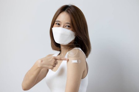 Photo for Vaccinated asian young woman with face mask pointing at vaccine shot bandage - Royalty Free Image