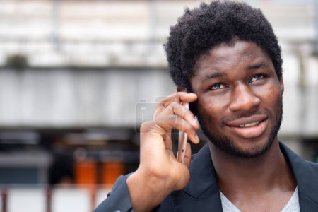 Téléchargez les photos : Heureux homme d'affaires africain souriant parlant, négociant via smartphone - en image libre de droit