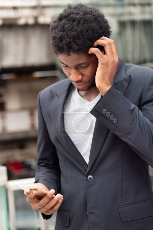 Téléchargez les photos : Contrarié homme d'affaires africain ou employé de bureau ayant du mal à utiliser l'application smartphone - en image libre de droit
