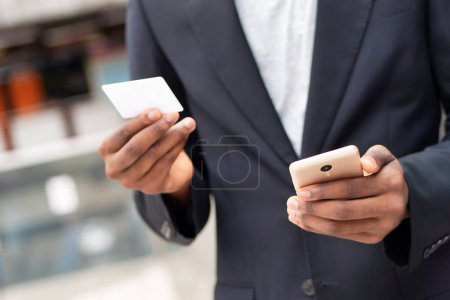 Téléchargez les photos : Homme d'affaires africain utilisant smartphone et carte de crédit pour la transaction électronique en ligne - en image libre de droit