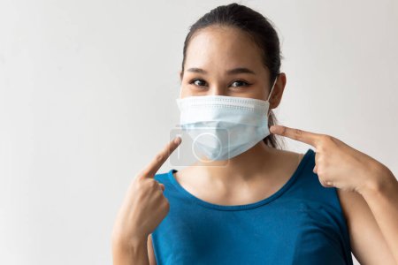 Téléchargez les photos : Femme heureuse portant et pointant vers le masque facial pour la protection contre la grippe saisonnière et la pollution par la poussière - en image libre de droit
