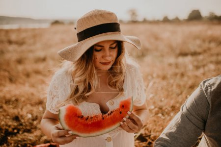 Photo for Happy European caucasian pregnant woman relaxing in nature picnic eating fruit red juicy watermelon laugh having fun. expectant mother in hat and dress eating watermelon in summer. face with moles - Royalty Free Image