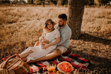 Photo for Happy European caucasian family with a pregnant woman relaxing in nature picnic hug laugh having fun. expectant mother in hat and dress in summer. face with moles - Royalty Free Image