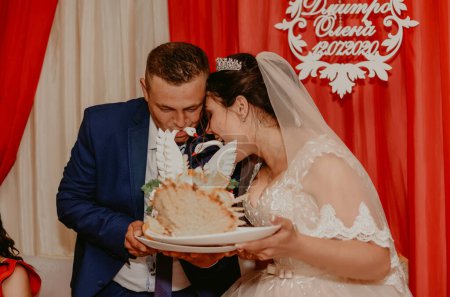 Bräutigam und Braut in Schleier nehmen einen Bissen der traditionellen ukrainischen Hochzeitstorte korovai slawisch ukrainisch-russisch Traditionen