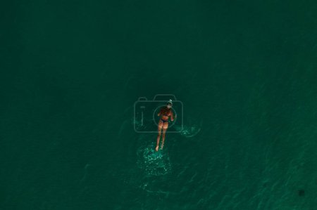 Aerial top nature view above green turquoise Thracian sea Greece Ellada. Beautiful young woman bikini swimming alone middle ocean water. girl in diving mask for snorkeling. wide panoramic view marine