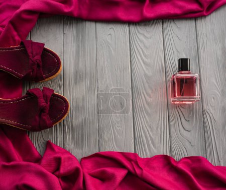 burgundy sandals wedge shawl shoes and bottle pink perfume. Summer background template mockup copy free space pattern colorful composition sample text. Top view above grey wooden background flat lay