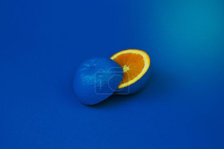 Photo for Modern art piece featuring a halved orange with the rind painted blue on a blue background. - Royalty Free Image