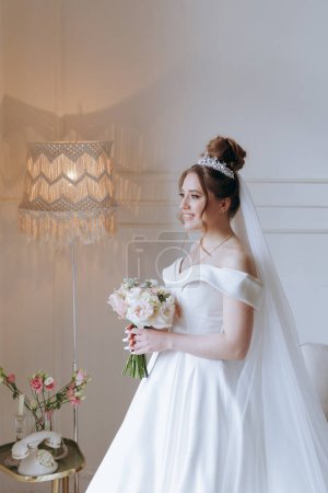Foto de Los preparativos de la mañana de una novia hermosa y sexy en un albornoz en el balcón y en el sofá, donde se pone los zapatos en un vestido de novia - Imagen libre de derechos